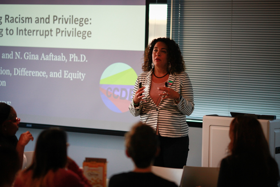 Dr. Ralina Joseph speaking in front of an Interrupting Privilege slide